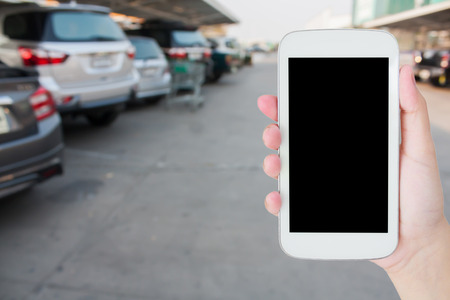 hand holding mobile phone with blur car park backgroundの写真素材