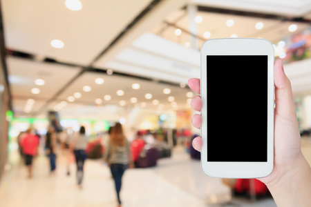 hand hold mobile phone with blurred shopping mall backgroundの写真素材