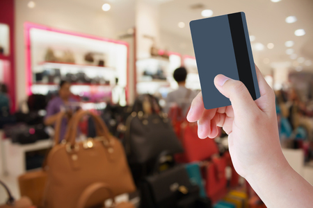 Female hand holding credit card with shopping mall backgroundの写真素材