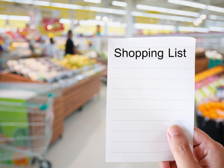 Female hand holding shopping list paper on grocery store blur backgroundの写真素材