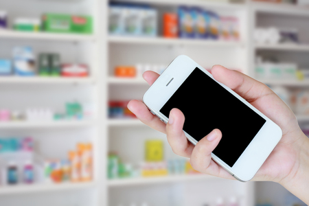 pharmacist hand holding smart phone with blur some shelves of drug in the pharmacy drugstoreの写真素材