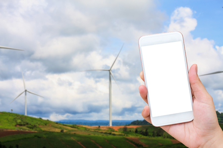 hand holding mobile phone with wind turbines background, renewable energyの写真素材
