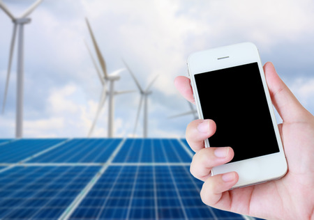 hand holding mobile phone with solar panels and wind turbines background, renewable energyの写真素材