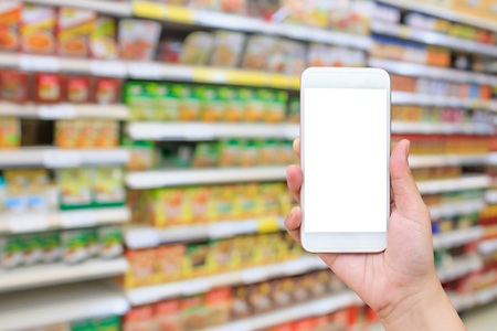 female hand holding mobile smartphone over supermarket blur background, shopping online business conceptの写真素材