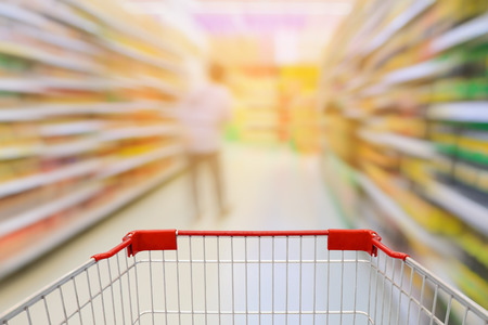 Supermarket aisle with empty red shopping cartの写真素材