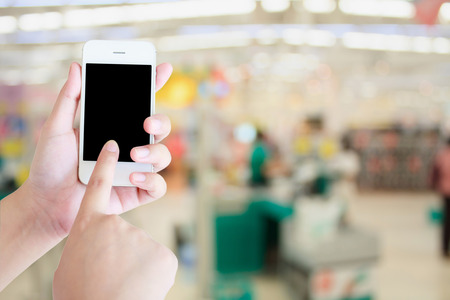 hand hold smartphone with Supermarket store background ,Cashier counter with customerの写真素材