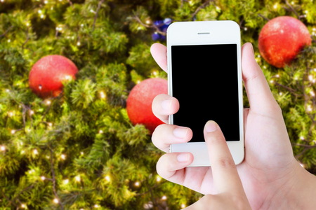 Christmas party concept - hand holding mobile smart phone with Christmas lights bokeh on Xmas treeの写真素材