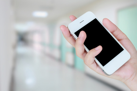 hand holding smartphone with hospital interior corridor blurred backgroundの写真素材