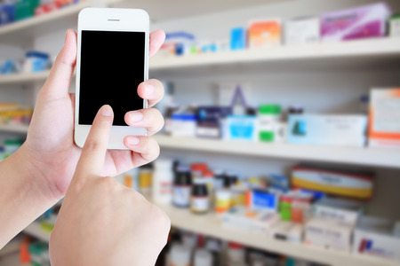 pharmacist hand holding smart phone with blur some shelves of drug in the pharmacy drugstoreの写真素材