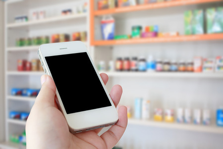 pharmacist hand holding smart phone with blur some shelves of drug in the pharmacy drugstoreの写真素材