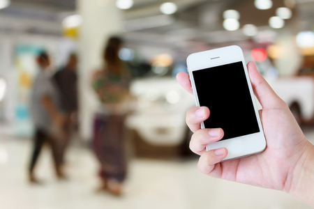 hands holding mobile phone with new cars in showroom dealershipの写真素材