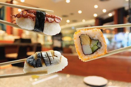 sushi in chopsticks with japanese restaurant interior blurred backgroundの写真素材