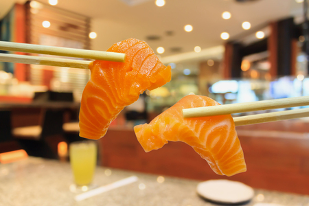 salmon sashimi in chopsticks with japanese restaurant interior blurred backgroundの写真素材