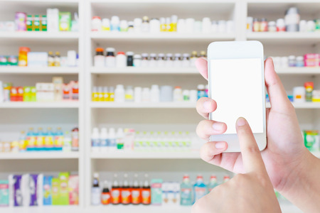 female hold mobile smartphone in the pharmacy blurred background, Pharmacist using smartphone in the pharmacyの写真素材
