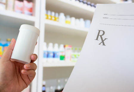 closeup hand of female pharmacist with prescription and medicine bottle at the pharmacyの写真素材