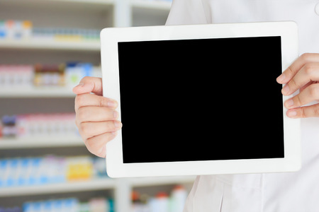 pharmacist showing blank digital tablet computer with shelves of drugs in the pharmacy storeの写真素材