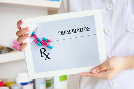 Female pharmacist showing tablet computer with prescription and medicine capsules on screen over pharmacy drugstore backgroundの写真素材