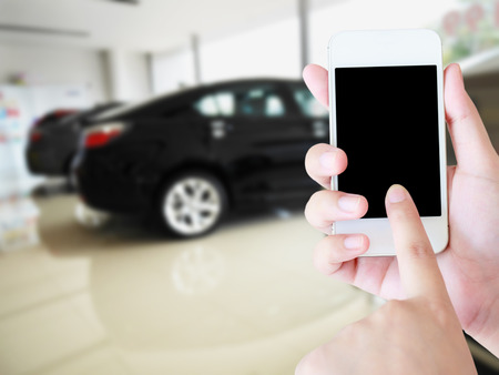 woman hands holding mobile phone with blurred background of new cars in car showroom, buying new car conceptの写真素材