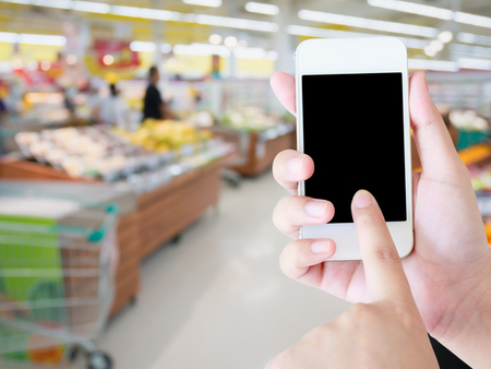 Female hand holding mobile phone on grocery store blur backgroundの写真素材