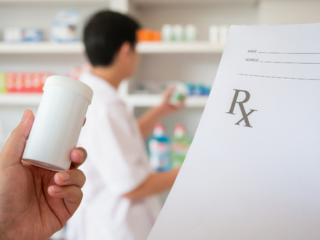 closeup hand of female pharmacist with prescription and medicine bottle at the pharmacyの写真素材