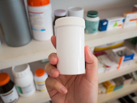 Close up pharmacist hand hold medicine bottles on shelves of drugs in the pharmacy, Pharmacy drugstore blurred backgroundの写真素材