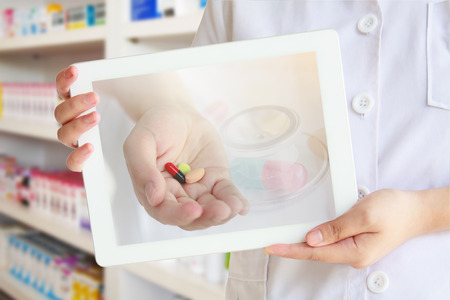 Female pharmacist showing tablet computer with medicine on screen over pharmacy drugstore backgroundの写真素材