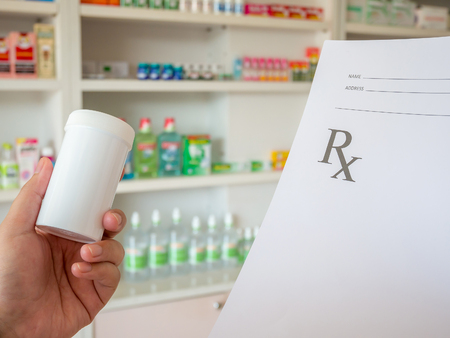 closeup hand of female pharmacist with prescription and medicine bottle at the pharmacyの写真素材