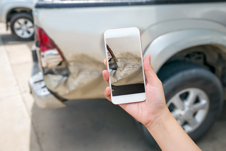 woman using smart phone to take car damage photo caused by car crash accident, car insurance conceptの写真素材