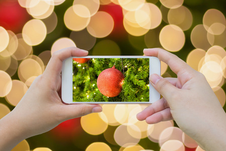 Female using mobile smart phone Taking photo of Christmas decoration on christmas tree with bokeh light backgroundの写真素材