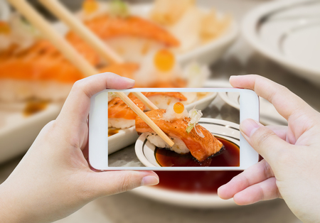 Taking photo of Grilled salmon sushi in chopsticks, japanese cuisine