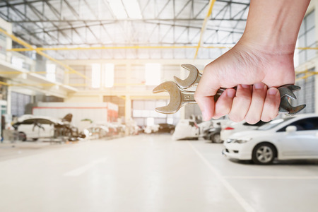 Auto mechanic hand holding wrench over car repair service centre garageの写真素材