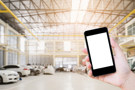 Female hand holding mobile smart phone on car service centre or garage blur backgroundの写真素材