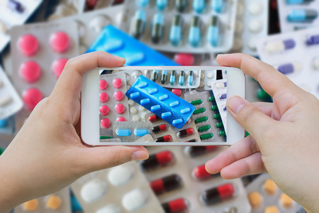 Female hand hold mobile smart phone taking photo of medicine pillsの写真素材
