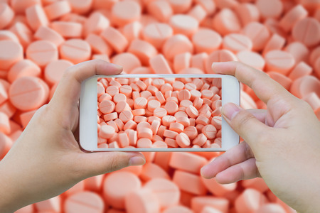 Female hand hold mobile smart phone taking photo of medicine pillsの写真素材