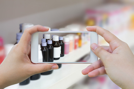Female hand hold mobile smart phone taking photo of medicine bottles on the pharmacy store shelvesの写真素材