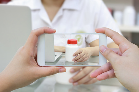 Female hand hold mobile smart phone taking photo of medicine bottle in the pharmacyの写真素材