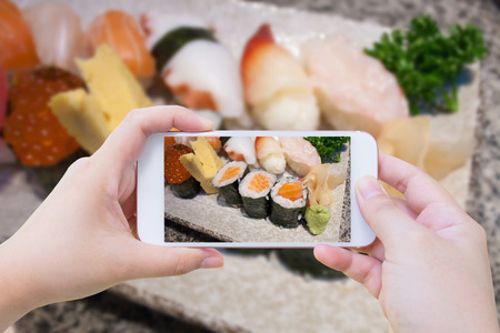 Female using mobile smart phone Taking photo of Japanese sushi setの写真素材