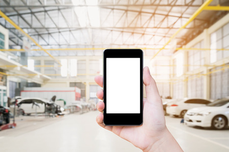Female hand holding mobile smart phone on car service centre or garage blur backgroundの写真素材
