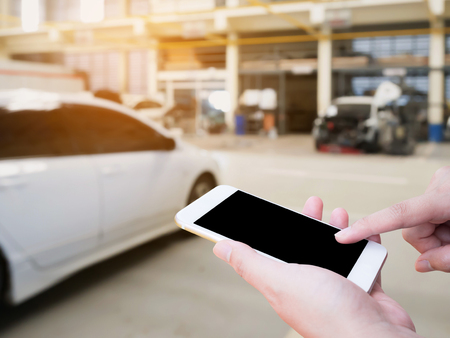 Female hand holding mobile smart phone on car service centre or garage blur backgroundの写真素材