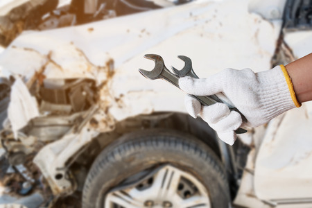 mechanic hand hold wrench with car crash accident damage background, auto body repair conceptの写真素材
