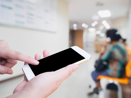 hand hold mobile smartphone with blur hospital interior for backgroundの写真素材