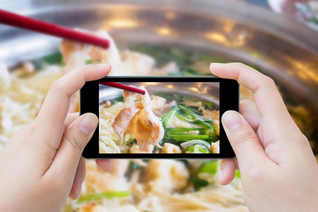 woman taking photo of sukiyaki shabu shabu with mobile smartphoneの写真素材