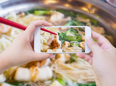 woman taking photo of sukiyaki shabu shabu with mobile smartphoneの写真素材