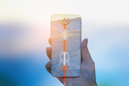 hand hold mobile smartphone double exposure with telecom tower, telecommunication conceptの写真素材