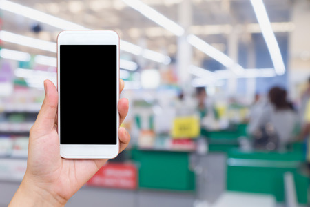 Woman hand holding mobile phone at supermarket checkout background, digital wallet conceptの写真素材