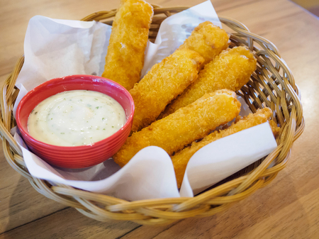 fresh fish fingers sticks with sauce in basket on wood tableの写真素材