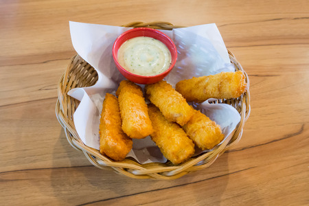 fresh fish fingers sticks with sauce in basket on wood tableの写真素材