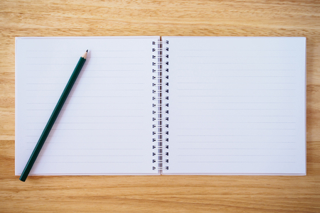 blank white notebook top view with pencil on brown wood desk table backgroundの写真素材