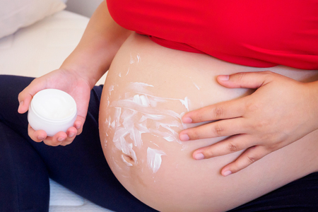 Pregnant Woman applying stretch marks cream on her bellyの写真素材