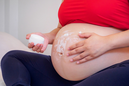 Pregnant Woman applying stretch marks cream on her bellyの写真素材